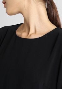 Sort bluse med en bred, rund halsudskæring. Glat tekstur, korte ærmer og en afslappet pasform. Minimalistisk design uden synlige dekorationer.