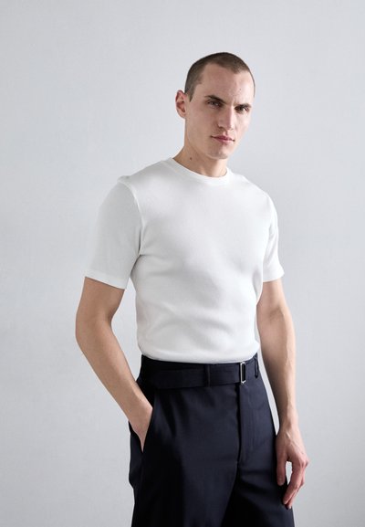 T-shirt blanche à manches courtes en maille côtelée associée à un pantalon noir ajusté, agrémenté d'une ceinture simple. Tissu lisse dans un design ajusté.