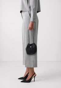 Borsa a secchiello nera con finitura testurizzata e dettaglio del logo metallico, abbinata a pantaloni a quadri a vita alta e décolleté neri a punta.