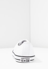 Hvitt lerret lavt snøresko med svart gummisåle og striper, med "Converse All Star" logo på hælen.