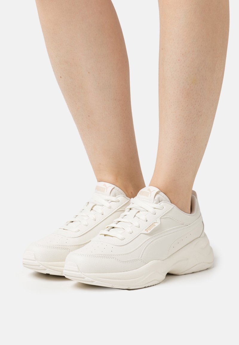 Białe skórzane sneakersy z masywną podeszwą, sznurowanym zapięciem, perforowanymi detalami oraz delikatnym logo po bokach i na języku.