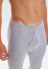 Grey cotton leggings with a fitted design, featuring a waistband and a front pouch for support. Smooth texture and stretchable fabric.