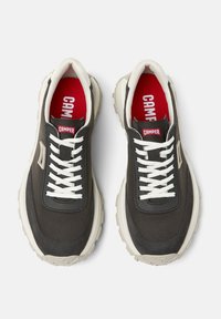 Zapatillas negras y grises con cordones blancos y una suela gruesa color beig. Cuenta con un logo rojo de "CAMPER" en la plantilla y acentos laterales.