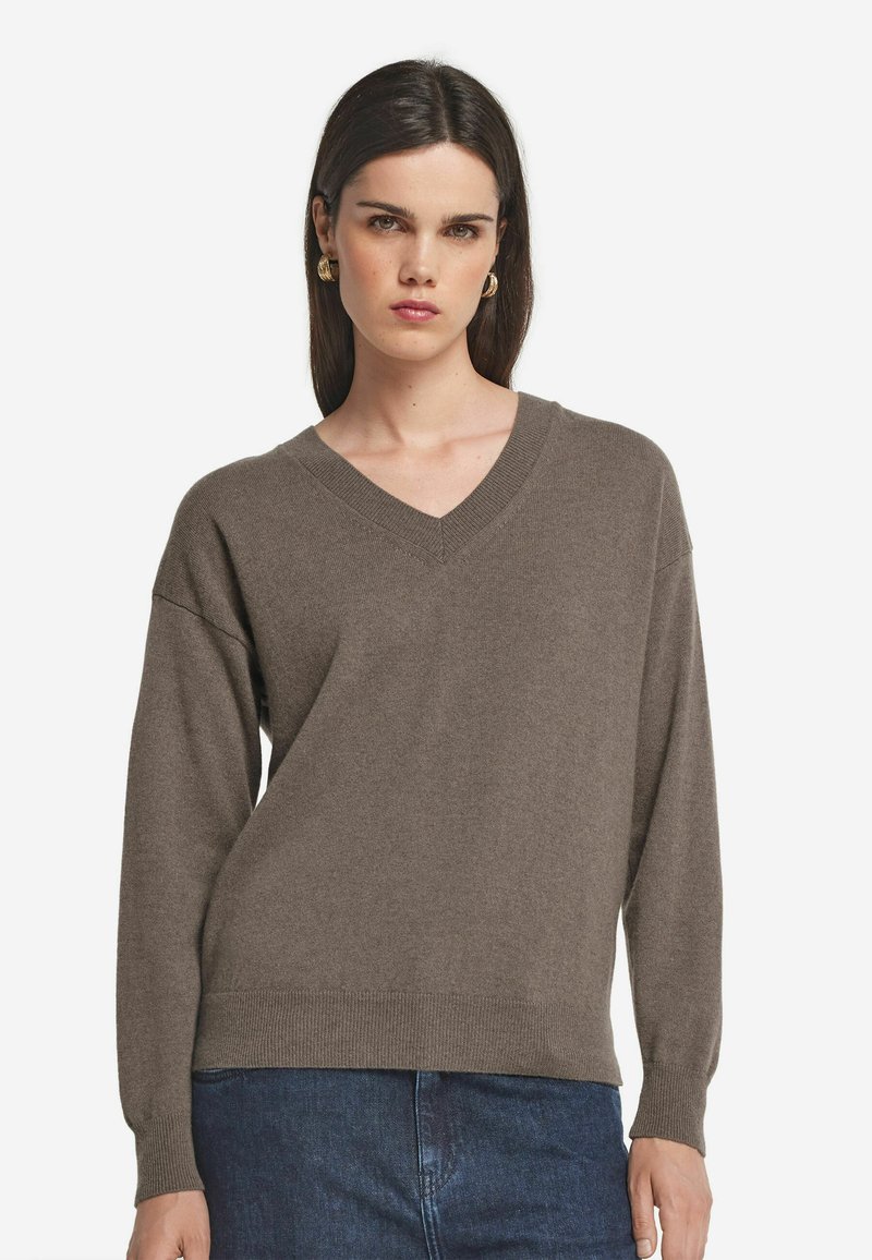 V-Ausschnitt, langärmliger Pullover in einem gedämpften Braunton, aus weichem Strickstoff mit gerippten Bündchen und Saum. Kombiniert mit dunkler Denim.