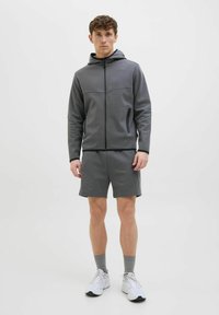 Siva zip-up dukserica s kapuljačom i kengur džepom; uparen sa odgovarajućim šortsom. Tkanina izgleda glatko, pogodna za sportsku odjeću.