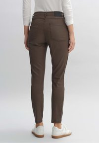 Ruske slim-fit hlače s dva stražnja džepa, crnim remenom i bijelim tenisicama, prikazane straga na svjetloj pozadini.