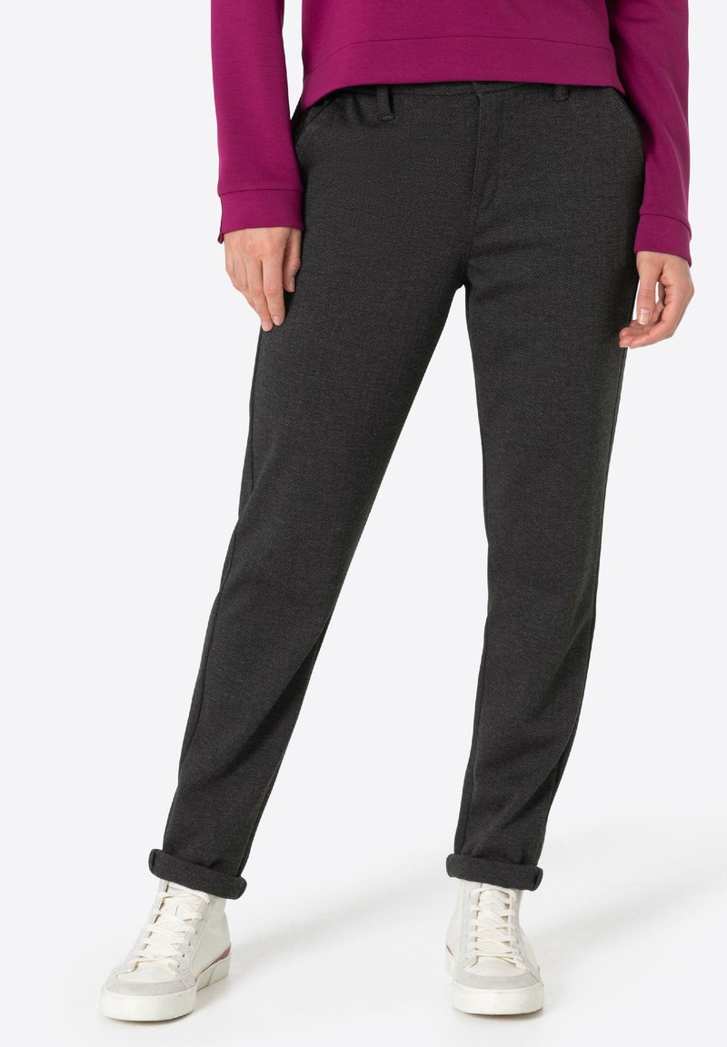 Dark gray tailored pants with a textured finish, featuring a fitted waist and rolled cuffs. Paired with white lace-up sneakers.