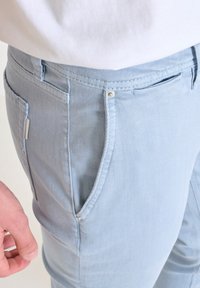 Svijetloplave traperice s teksturiranim završetkom, opremljene prednjim džepovima, metalnom gumbom i minimalističkim detaljima šivanja.