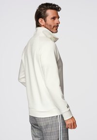 Sudadera de forro polar blanco con cuello alto, que presenta una superficie texturizada. Acentuada por un logotipo de la marca bordado en la manga. Ajuste cómodo.
