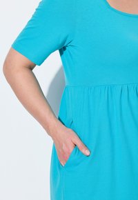 Vestido turquesa con mangas cortas, corpiño ajustado y cintura fruncida. Presenta bolsillos laterales, tejido suave y escote redondeado.