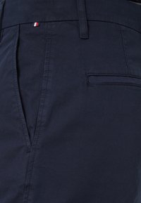 Granatowe bawełniane spodnie o gładkiej fakturze, z tylną kieszenią i małym akcentem w postaci trójkolorowej flagi w pobliżu pasa.