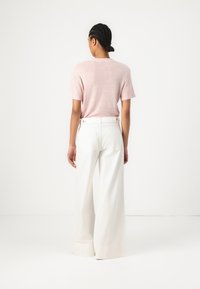 T-shirt rosa chiaro a maniche corte abbinato a pantaloni larghi bianchi a vita alta, caratterizzati da una texture liscia e due tasche posteriori.