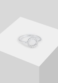Anello in argento con design circolare decorato con piccole pietre trasparenti, finitura lucida e una fascia sottile e liscia.