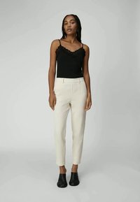Zwarte tanktop met kantafwerking, gecombineerd met crèmekleurige tapered broek en zwarte instappers. Soepele textuur, aansluitend ontwerp en subtiele tailoring.