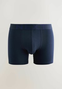 Námorníckomodré pánske boxerky s elastickým pásom s logom "NEXT" na svetlom jednoduchom pozadí.