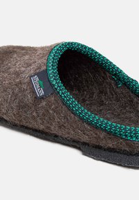 Brown felt slipper featuring a textured wool body, a green woven trim, and a rubber sole for grip. Includes a brand tag on the side.