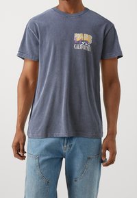 Navy blue cotton t-shirt with short sleeves, featuring a front graphic that reads “BIG SUR CALIFORNIA” in yellow and purple text.