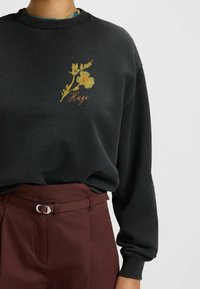 Svart sweatshirt med en blommig broderadesign i gult och grönt, med rund halsringning och ribbade ärmslut. Matchas med vinröda byxor.