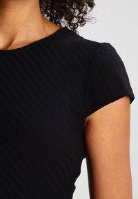 Black ribbed dress with short sleeves and a rounded neckline, showcasing a textured fabric and a sleek silhouette.