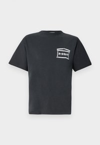 Fekete pamut póló kerek nyakkivágással és rövid ujjal, a bal oldali mellzseb területén fehér grafikai kialakítással.
