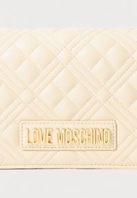Kremasti kviltani kožni ruksak s zlatnom pločicom "LOVE MOSCHINO" koja se nalazi u sredini prednje strane.