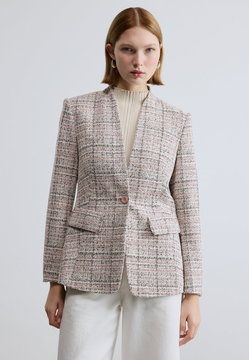 Tweedblazer i pastelrosa og sort ternet mønster med enkelt knaplukning, hakkrave og forlommer. Bæres over en ribbet top.