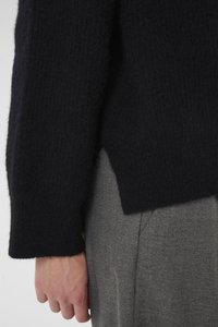 Black knitted sweater with a textured finish, featuring a relaxed fit and ribbed sleeves, paired with gray tailored trousers.