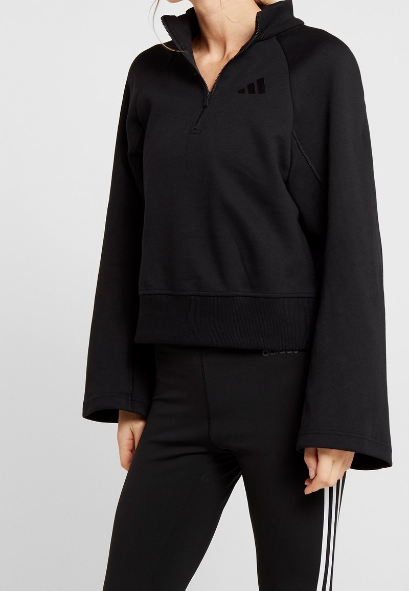 Sweatshirt noir court avec fermeture éclair quart, manches larges et ourlet côtelé. Présente un logo ton sur ton sur la poitrine et un tissu texturé.