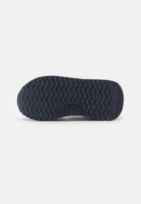 Semelle en caoutchouc bleu marine avec un motif de gomme ondulé et des accents en relief. Comprend un logo gravé sur le talon.