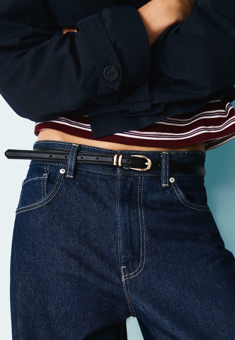 Črn usnjen pas z zlatim zaponko, nosen čez temno modre jeans hlače s kontrastnim šivom. Obleka vsebuje mornarsko jakno in črtasto srajco.