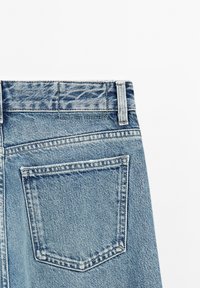 Světle modré džíny z denimu s vysokým pasem, vybavené zadní kapsou a kontrastním prošitím. Látka má mírně texturovaný povrch.