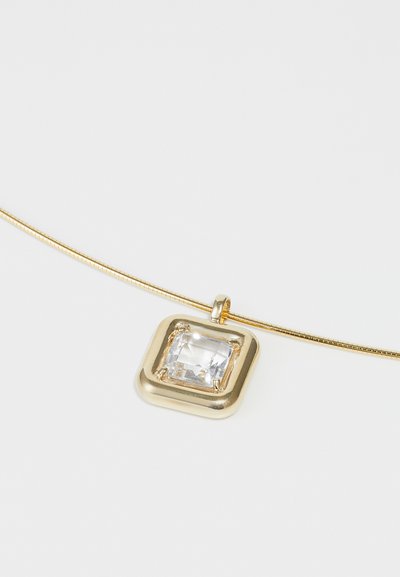 Collana d'oro con pendente quadrato decorato con una pietra gemma trasparente e sfaccettata incastonata in una cornice d'oro liscia. La catena è sottile e elegante.