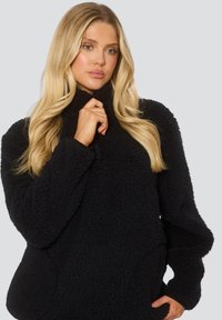 Pullover in pile nero con superficie testurizzata, colletto alto e chiusura con zip. Caratterizzato da un fit rilassato e maniche lunghe.