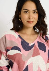 Jersey de cuello en V con manga larga en rosa, con patrones abstractos en blanco, azul marino y burdeos. Tejido texturizado con un acabado suave y colores contrastantes.