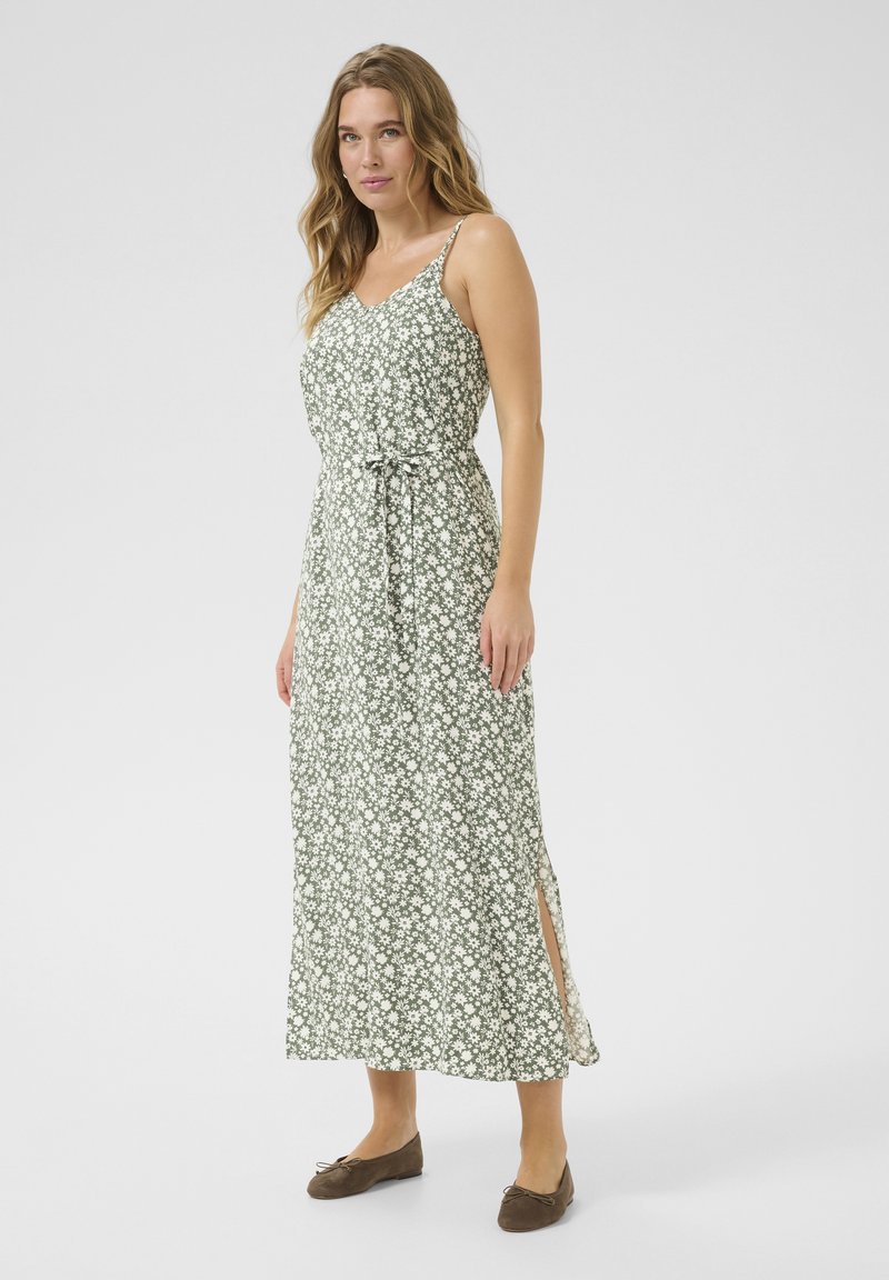 Groene bloemen maxi-jurk met spaghettibandjes, cinched taille, zijsplitten en witte bloemenpatronen; gecombineerd met bruinere slippers.