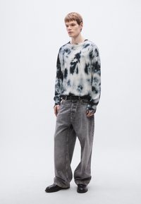 Μπλουζάκι φούτερ tie-dye σε ασπρόμαυρο χρώμα με λογότυπο, συνδυασμένο με άνετο γκρι τζιν παντελόνι και μαύρα παπούτσια. Απλός, καθημερινός σχεδιασμός ρούχου.