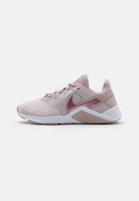 Zapatilla deportiva rosa claro con textura hexagonal, tela suave y suela blanca. Presenta un logotipo sutil y acentos brillantes en rosa más oscuro.