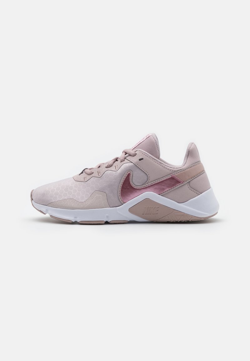 Zapatilla deportiva rosa claro con textura hexagonal, tela suave y suela blanca. Presenta un logotipo sutil y acentos brillantes en rosa más oscuro.