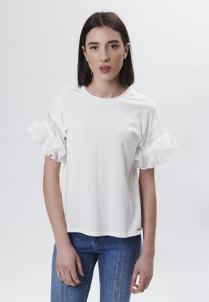 Camiseta blanca con mangas de rayas con volantes. Tela suave, escote redondo, ajuste relajado. Combinada con jeans azules, diseño minimalista.