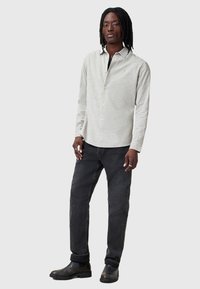 Lys grå skjorte med krave, parret med mørke jeans og sorte ankelstøvler, med en afslappet pasform og minimalistisk design.