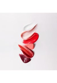 Smears of makeup cream or lipstick in white, pale pink, bright red, coral, deep red, and plum shades on a white background.