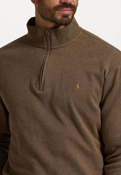 Brun kvartdragspullover, ribbad textur, tillverkad av mjukt tyg, med en liten broderad logotyp på bröstet och en hög krage.