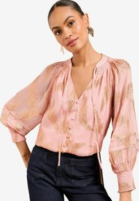 Rosa Bluse mit goldenen Blattmustern, Knopfverschluss und V-Ausschnitt. Verfügt über luftige Ärmel mit elastischen Bündchen und gerafften Details.