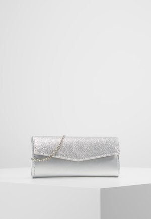 Zilveren clutch met glinsterende klep en dunne kettingband, tentoongesteld op een wit voetstuk tegen een effen grijze achtergrond.