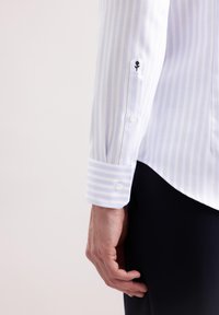 Jasnoniebieska koszula w paski, biała, z guzikami na mankietach oraz haftowanym detalem kwiatowym na rękawie. Gładka struktura materiału.