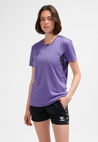 Lila atletisk t-shirt med korta ärmar och v-ringning. Svarta sidopaneler och hummerlogotyp på bröstet. Bärs med svarta shorts med ett mönster.