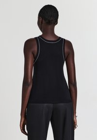 Top in maglia nera senza maniche con scollatura rotonda, caratterizzato da cuciture bianche a contrasto lungo le cuciture e una silhouette aderente.