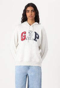 Sweatshirt à capuche gris clair avec un logo "G.A.P." multicolore ornée d'un motif paisley. Tissu doux, coupe ample et poche kangourou.