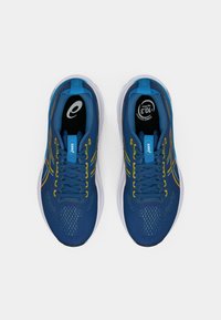 Chaussures de sport bleues avec un dessus en maille texturée, rayures accentuées jaunes, semelle blanche et semelles intérieures noires avec un logo. Design à lacets.