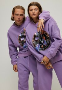 Paarse sweatshirts met een cirkelvormige grafiek van superhelden. De stof ziet er zacht uit, met bijpassende sweatpants en zilveren ringen om de handen.